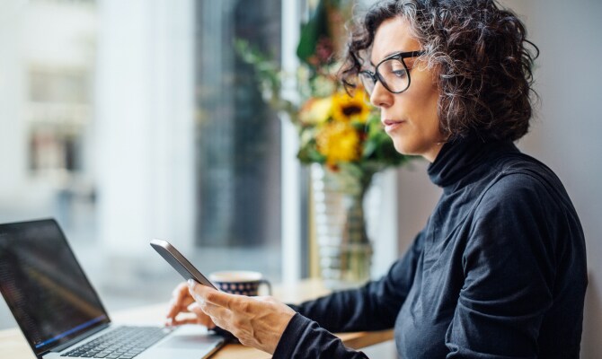 Una donna che guarda un telefono cellulare davanti a un computer portatile