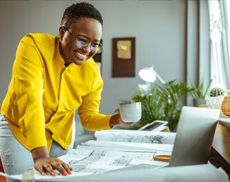 Una donna sorridente che guarda un computer portatile mentre tiene in mano una tazza